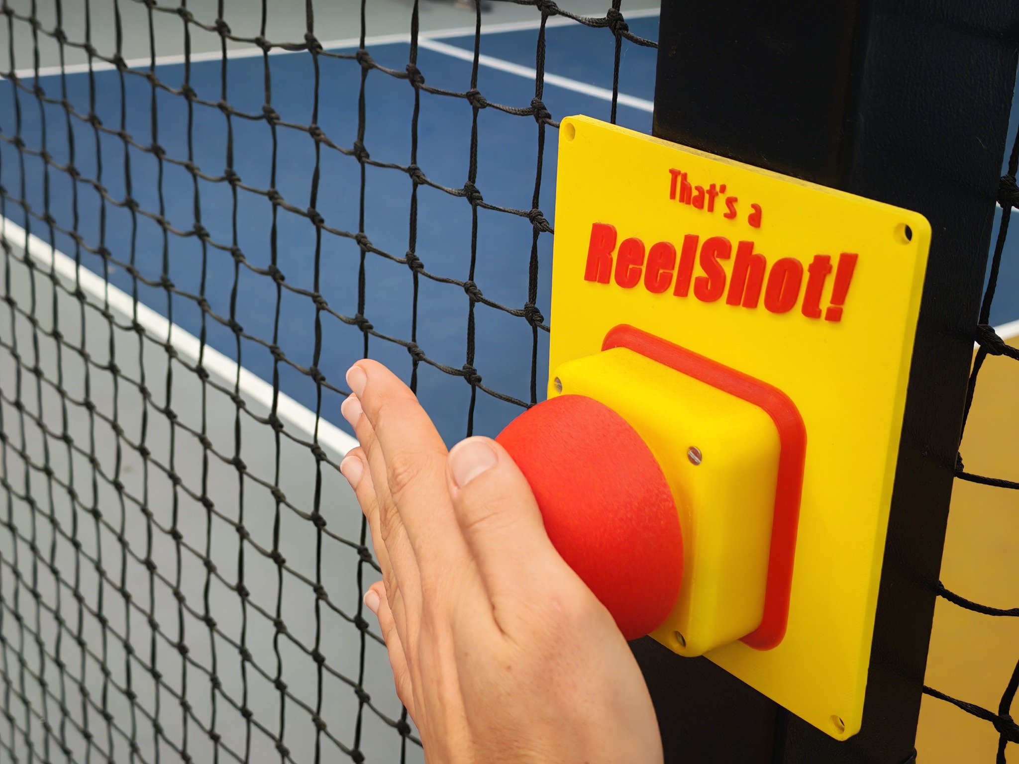 A hand pressing the red ReelShot button beside the court